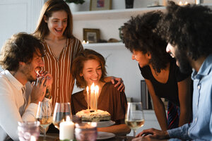 Freunde überraschen junge Frau mit einer Geburtstagstorte mit brennenden Kerzen - ERRF00598