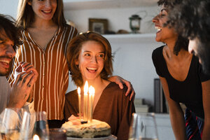 Freunde überraschen junge Frau mit einer Geburtstagstorte mit brennenden Kerzen - ERRF00599