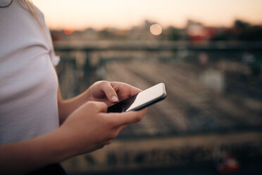 Midsection of young woman using smart phone while standing on bridge in city - MASF10297