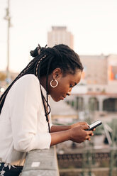 Side view of young woman text messaging through mobile phone while leaning on railing at bridge - MASF10302