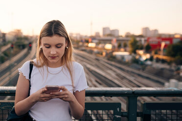 Junge Frau, die ihr Smartphone benutzt, während sie auf einer Brücke in der Stadt steht - MASF10307