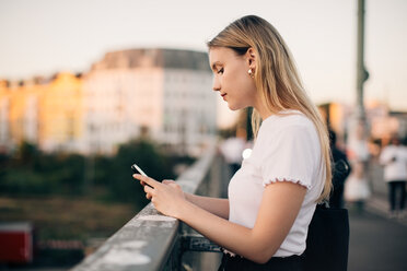 Side view of young woman using smart phone while standing on bridge in city - MASF10311