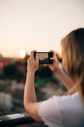 Ausgeschnittenes Bild einer jungen Frau, die den Fernsehturm bei Sonnenuntergang mit ihrem Smartphone fotografiert - MASF10316
