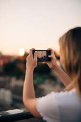 Cropped image of young woman photographing Fernsehturm through smart phone during sunset - MASF10316