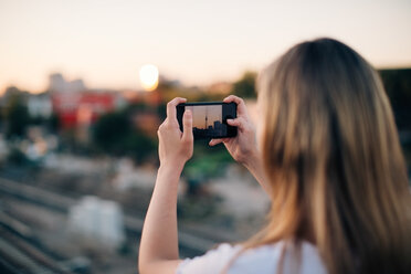 Junge Frau fotografiert den Fernsehturm während des Sonnenuntergangs mit ihrem Smartphone - MASF10317