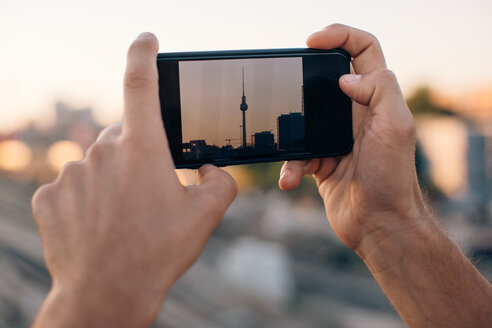 Ausgeschnittenes Bild eines jungen Mannes, der den Fernsehturm bei Sonnenuntergang mit seinem Smartphone fotografiert - MASF10325