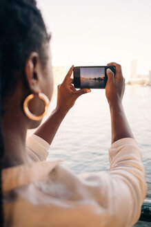 Ausgeschnittenes Bild einer jungen Frau, die mit ihrem Smartphone einen Fluss in der Stadt fotografiert - MASF10335