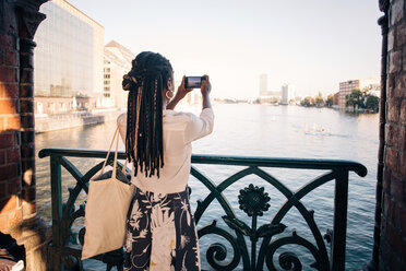 Rear view of young woman photographing river in city - MASF10338