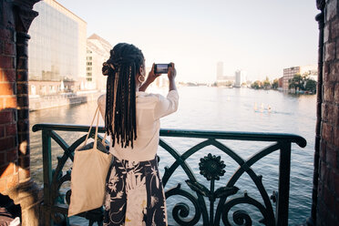 Rückansicht einer jungen Frau, die einen Fluss in der Stadt fotografiert - MASF10338