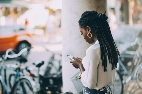 Junge Frau benutzt ihr Smartphone, während sie auf einem Fußweg in der Stadt steht - MASF10340