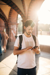 Junger Mann benutzt sein Smartphone, während er auf einem Fußweg in der Stadt steht - MASF10343