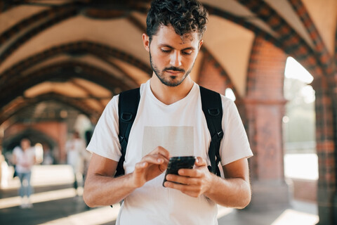 Junger Mann benutzt sein Smartphone, während er auf dem Gehweg steht, lizenzfreies Stockfoto