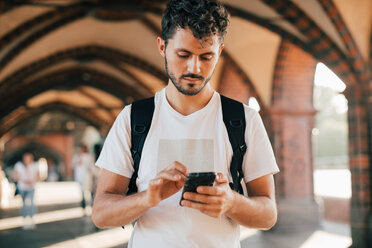 Young man using smart phone while standing on footpath - MASF10348