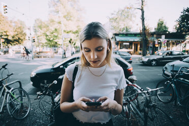 Junge Frau, die ein Mobiltelefon benutzt, während sie auf dem Gehweg in der Stadt steht - MASF10354