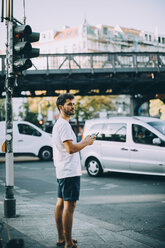 Seitenansicht eines jungen Mannes, der ein Mobiltelefon hält, während er auf dem Gehweg in der Stadt steht - MASF10362
