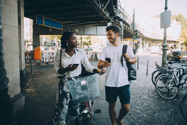 Lächelnde multiethnische Freunde unterhalten sich beim Gehen auf dem Bürgersteig in der Stadt - MASF10367