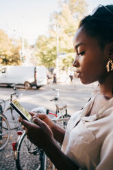 Young woman using smart phone while standing on sidewalk in city - MASF10370