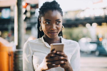 Young woman looking away while using mobile phone on street in city - MASF10376