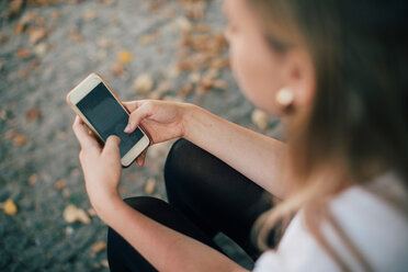 Hochformatige Ansicht einer jungen Frau, die ein Mobiltelefon benutzt, während sie auf einem Fußweg sitzt - MASF10381