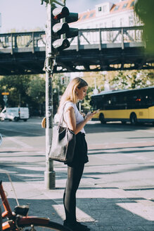 Seitenansicht einer jungen Frau, die ein Mobiltelefon benutzt, während sie auf dem Gehweg steht - MASF10386
