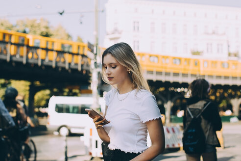 Junge Frau, die ein Mobiltelefon benutzt, während sie durch eine Straße in der Stadt läuft - MASF10387