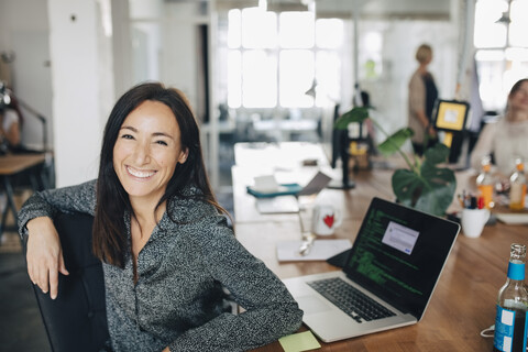 Porträt eines lächelnden weiblichen Computerprogrammierers, der in einem kreativen Büro am Schreibtisch sitzt, lizenzfreies Stockfoto