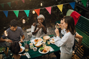 Hohe Winkel Ansicht der jungen Frauen fotografieren Freunde beim Essen während Dinner Party im Hinterhof - MASF10404