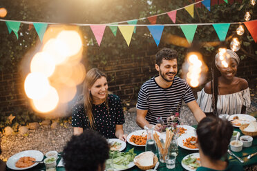 Glückliche multiethnische Freunde genießen das Abendessen am Tisch während einer Gartenparty - MASF10409