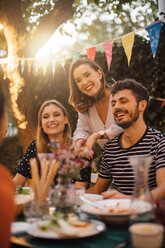 Happy young male and female friends at table during dinner party in backyard - MASF10410