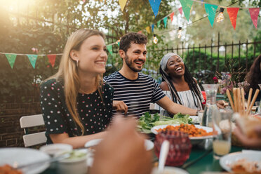 Glückliche multiethnische Freunde genießen das Abendessen am Tisch während einer Gartenparty - MASF10412