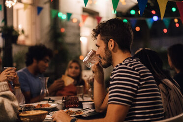 Junger Mann trinkt Wasser beim Abendessen mit Freunden während einer Gartenparty - MASF10425