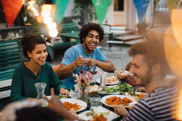 Cheerful male and female friends enjoying during dinner party in backyard - MASF10452