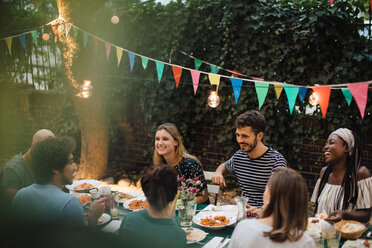 Multi-ethnic young friends enjoying dinner at table during garden party - MASF10454