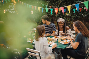 Young male and female friends enjoying food at table during dinner party in backyard - MASF10456