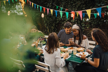 Junge männliche und weibliche Freunde mit Essen am Tisch während einer Dinnerparty im Hinterhof - MASF10457