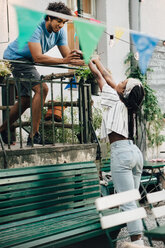 Young man giving food to female friend from balcony during garden party - MASF10465