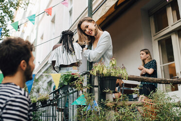 Smiling young woman looking at male friend while standing in balcony during garden party - MASF10486