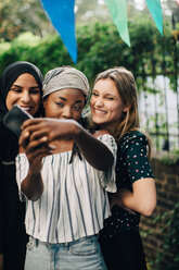 Glückliche multiethnische Freundinnen machen ein Selfie mit ihrem Handy im Hinterhof - MASF10505