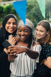 Glückliche multiethnische Freundinnen machen ein Selfie mit ihrem Smartphone im Hinterhof - MASF10506