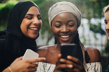 Glückliche multiethnische Freundinnen schauen auf ihr Handy, während sie im Hinterhof stehen - MASF10507