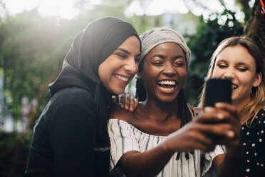 Lächelnde multiethnische Freundinnen machen ein Selfie mit dem Handy im Hinterhof - MASF10508