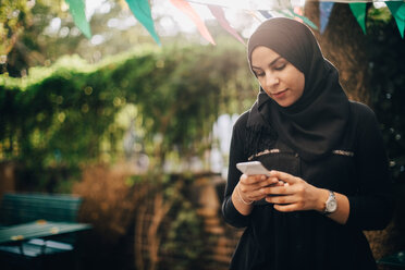 Junge Frau im Hidschab benutzt ihr Smartphone während einer Gartenparty - MASF10510