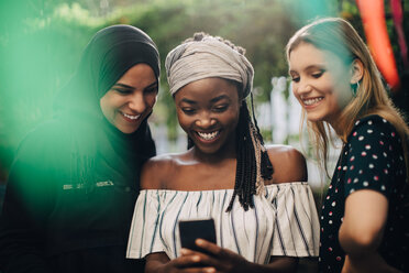 Lächelnde multiethnische Freundinnen schauen auf ihr Handy, während sie im Hinterhof stehen - MASF10511