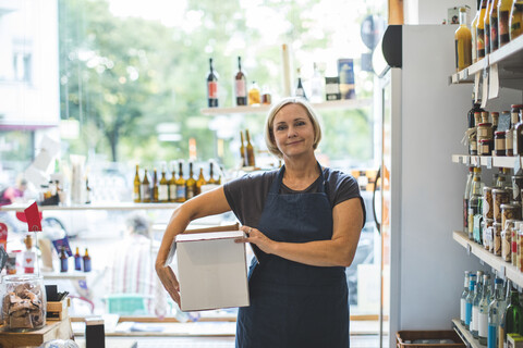 Portrait of confident female owner carrying cardboard box in deli stock photo