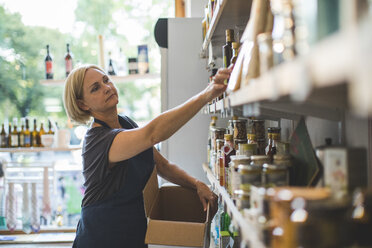 Mature female employee arranging bottles on shelf in deli - MASF10588