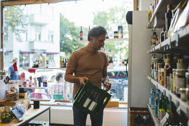 Mature salesman arranging bottle on shelf in deli - MASF10589