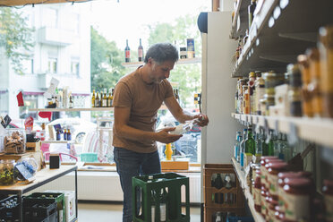 Salesman arranging bottle on shelf in deli - MASF10591