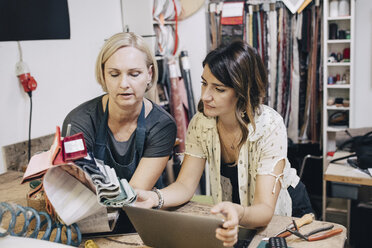 Female upholstery workers discussing over fabric swatch in workshop - MASF10607