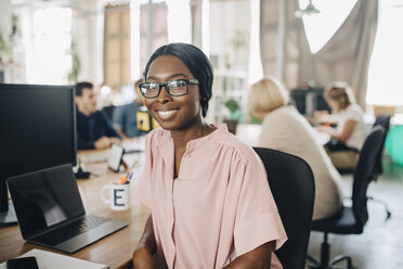 Portrait of smiling young businesswoman sitting at desk in creative office - MASF10663