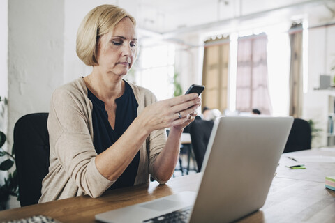 Mature businesswoman using mobile phone at desk in creative office stock photo